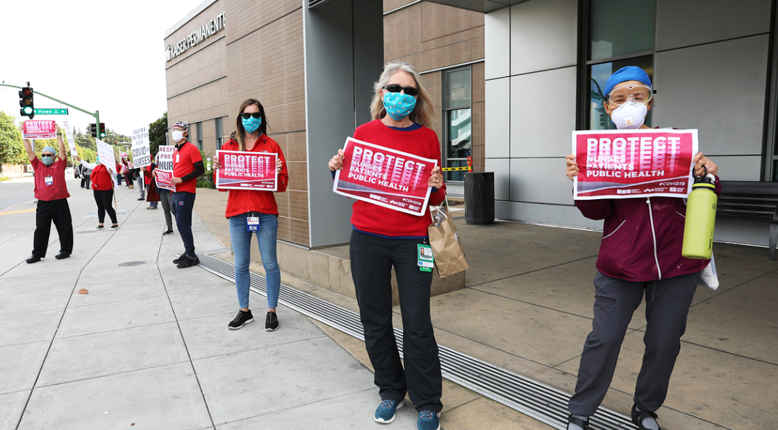 Nurses outside hospital hold signs "Protect Nurses, Patients, Public Health"