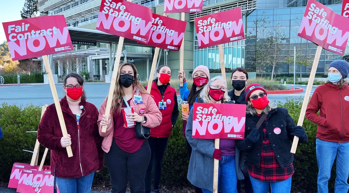 Group of nurses outside hold signs calling for safe staffing