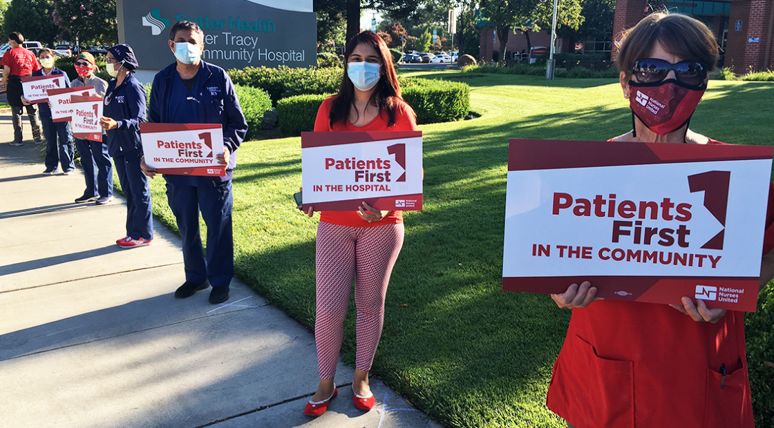 Nurses holding signs outside hospital "Patients first in the community"