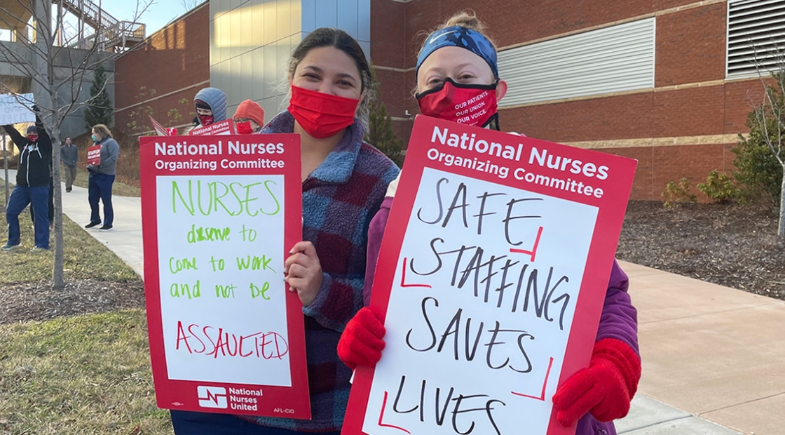 Two nurses outside holding signs calling for safe staffing and workplace violence prevention