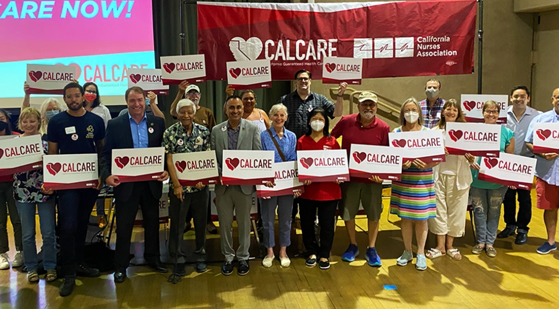 Large group of people standing in front of CalCare banner, holding CalCare signs
