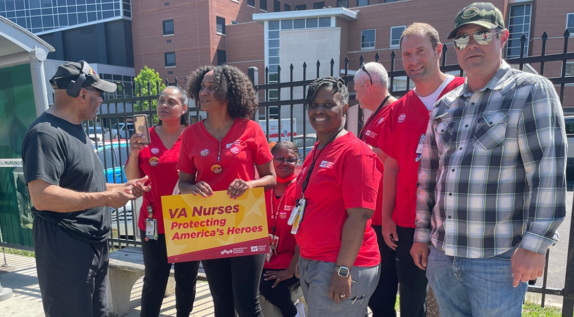 Group of VA nurses smiling, one holds sign "VA Nurses: Protecting America's Heroes"