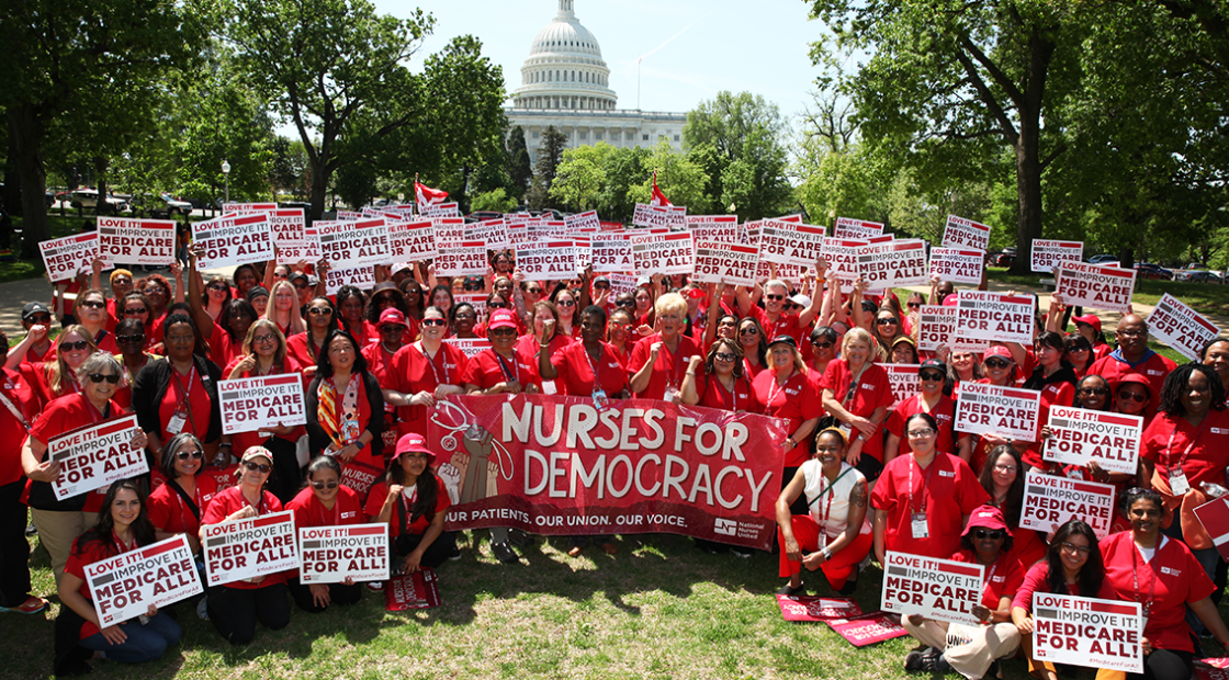 Large group of nurses in front of U.S. capitol with signs "Love it! Improve it! Medicare For All!"