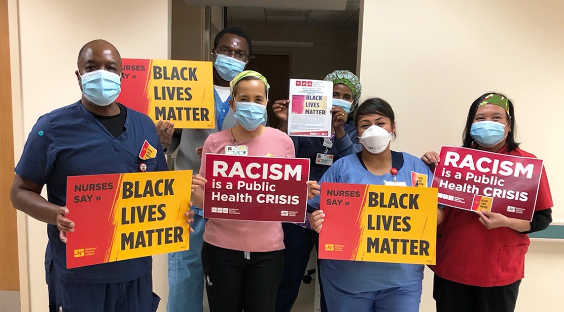 Group of nurses in hospital hold signs "Racism is a Public Health Crisis" and "Black Lives Matter"