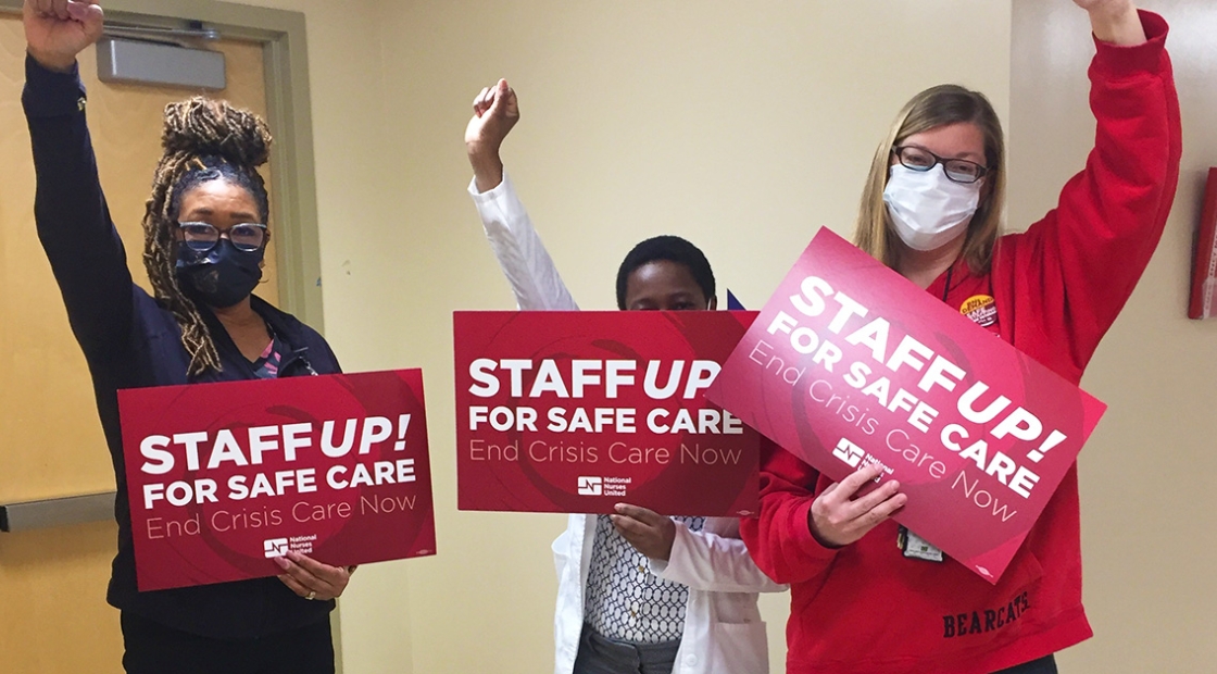 Three nurses with raised fists hold signs "Staff Up for Safe Care"