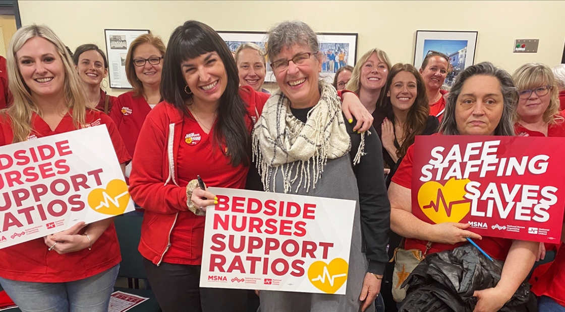 Group of smiling nurses holding signs "Bedside Nurses Support Ratios"
