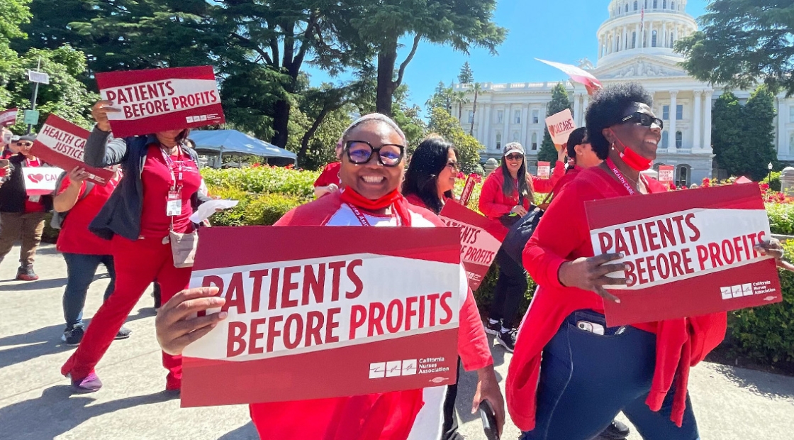 Nurses marching in front of California Capitol building holding signs "Patients Before Profits"