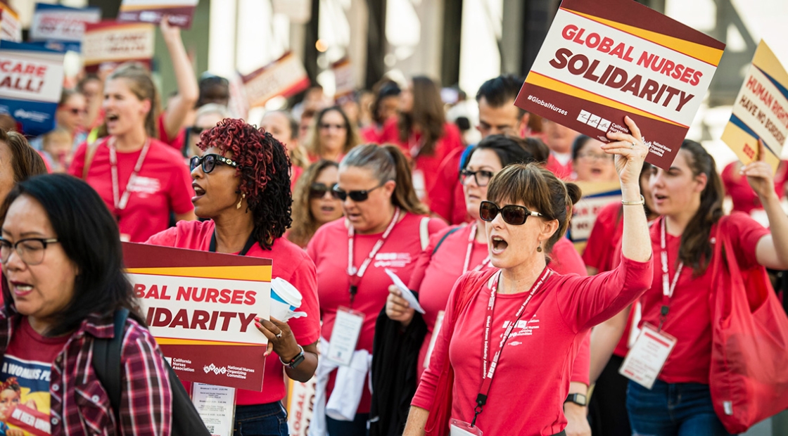 Nurses marching, holding signs "Global Nurses Solidarity"