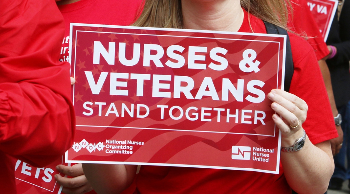Nurse holds sign "Nurses & Veterans Stand Together"