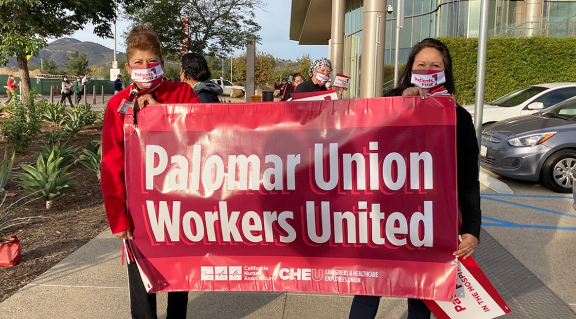 Two people outside hold sign "Palomar Union Workers United"