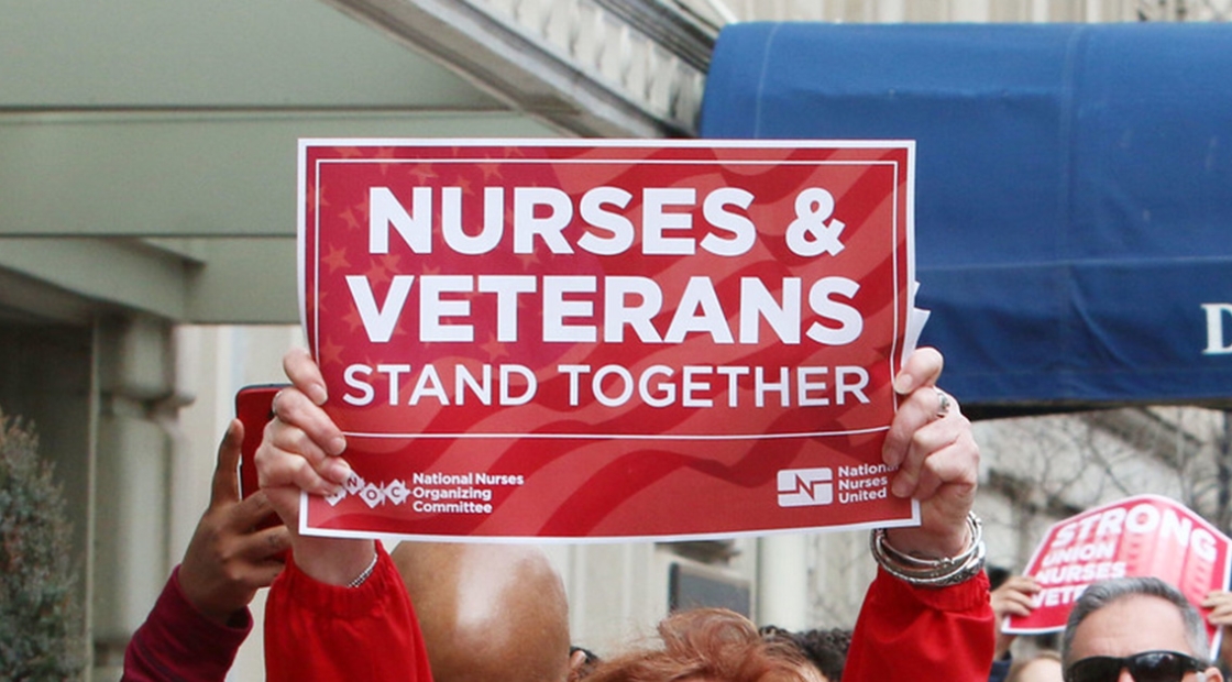 Nurse holds sign "Nurses & Veterans Stand Together"