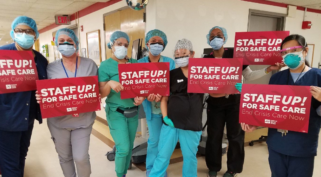 Group of nurses inside hospital hold signs "Staff up for safe patient care"