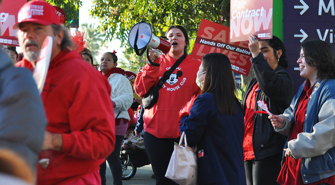 Long Beach nurses at action, with bullhorn, signs that say "Fair Contract Now" and "Save Lives: Hands off our Ratios!"