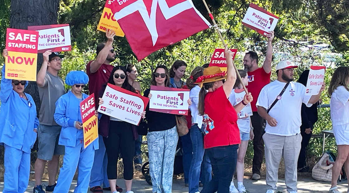 Nurses and community holding signs: "Safe staffing now" "Patients First in the hospital" "Patients First in the hospital" "Safe Staffing Saves Lives"