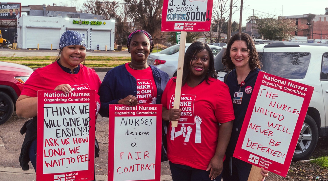 Four nurses standing outside smiling, holding signs calling for a fair contract