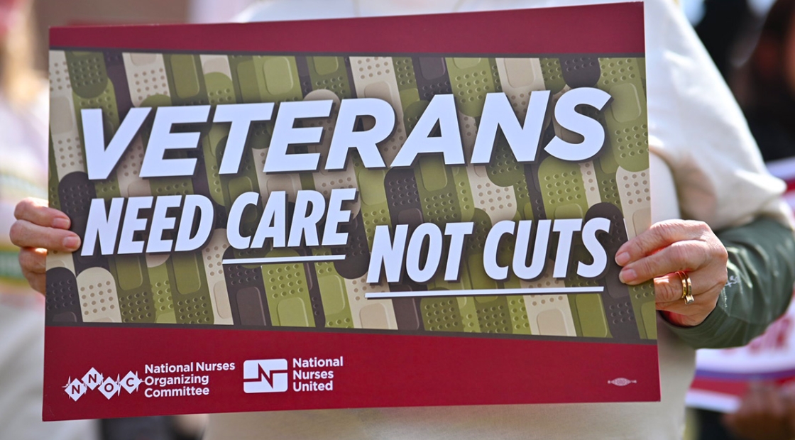 Hands holding sign "Veterans Need Care Not Cuts"