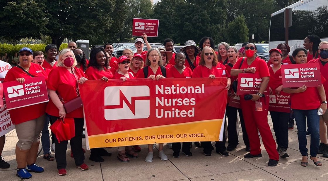 Large group of nurses holding "National Nurses United" banner in front of Washington Mounument