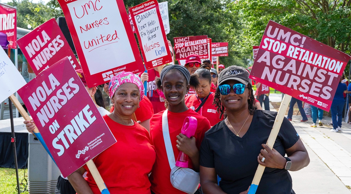Three nurses side-by-side, smiling, holding signs calling out LCMC Health