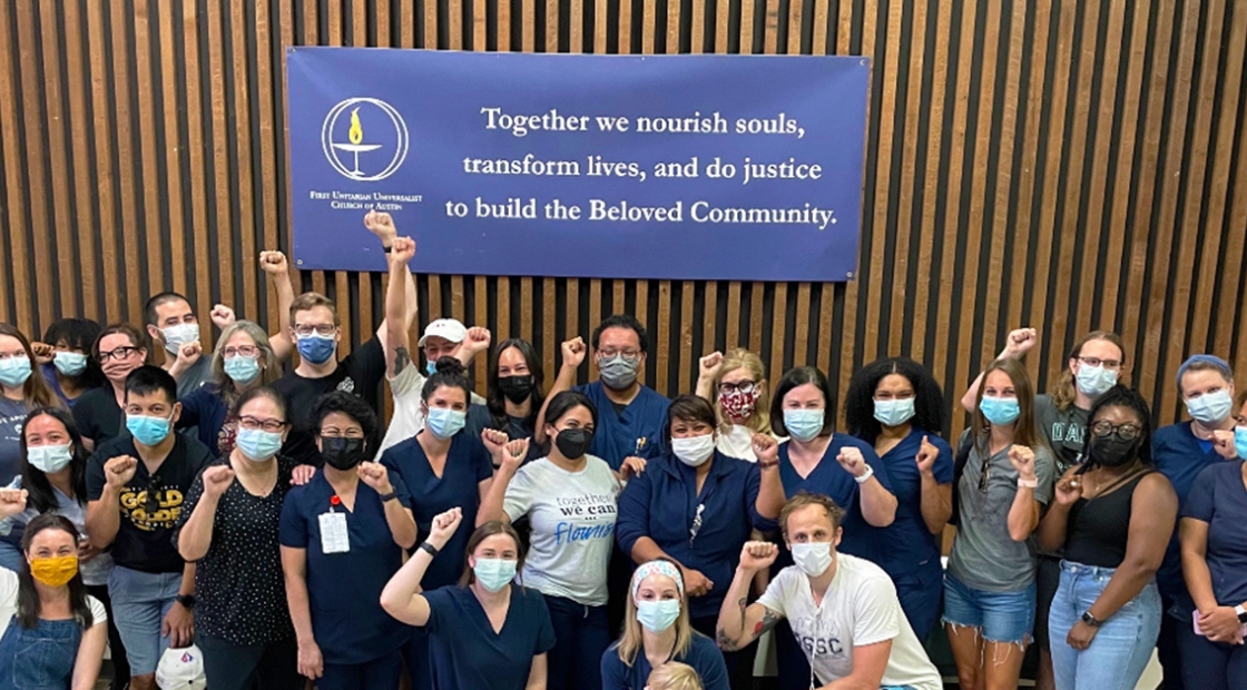 Large group of nurses with raised fists in front of sign "Together we nourish souls, transform lives, and do justice to build the Beloved Community