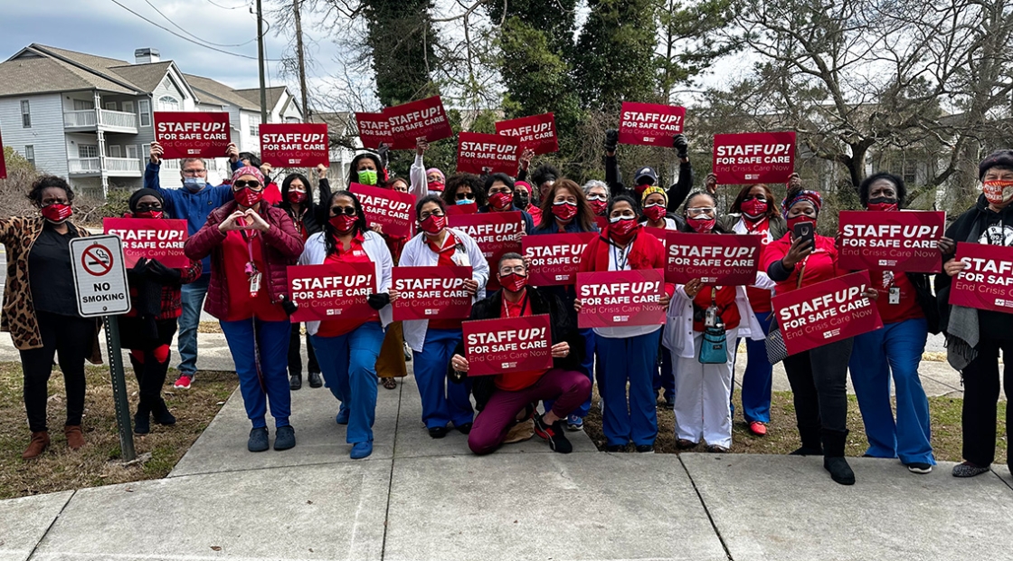 Large group of nurses outside holding signs "Staff Up for Safe Care"