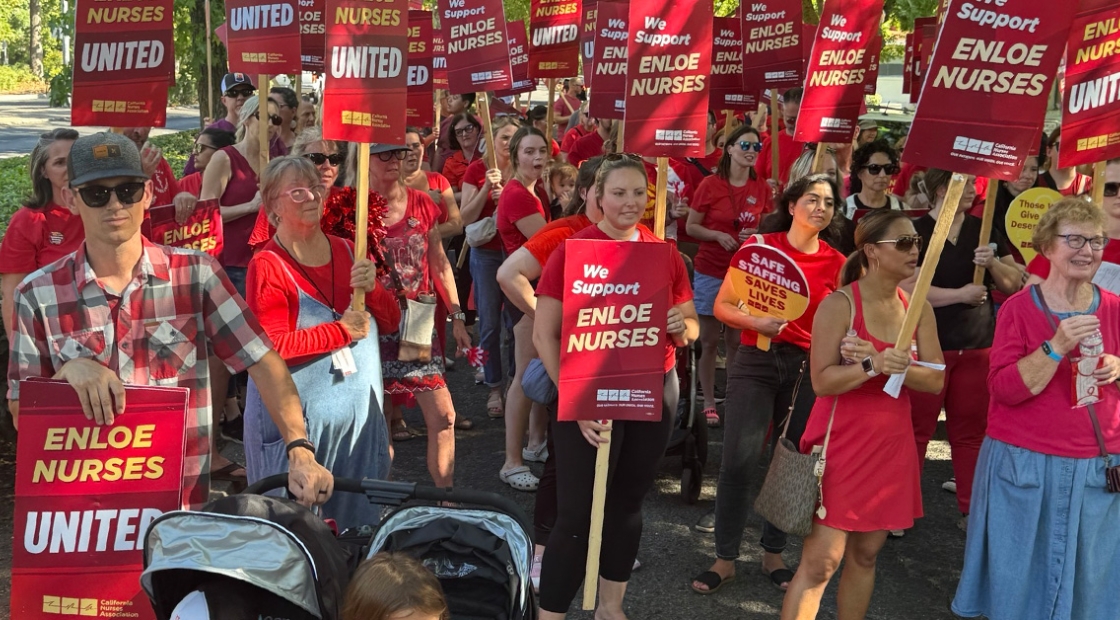 Large group of nurses outside holding signs "Enloe Nurses United"