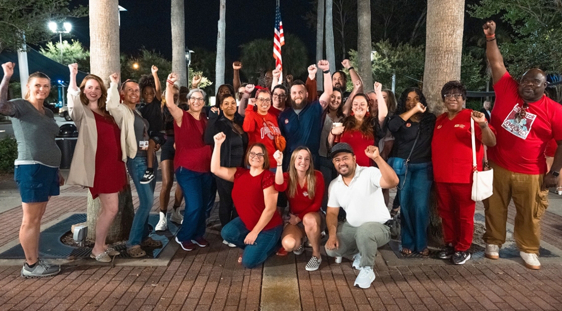 Large group of nurses outside, smiling, with raised fists