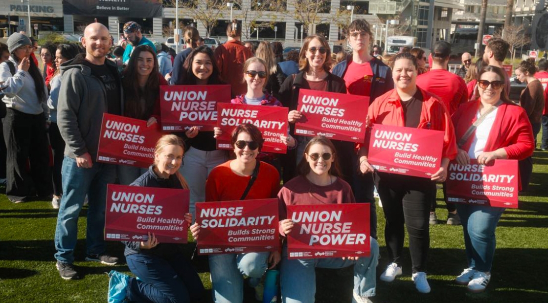 Group of nurses outside, smiling, holding signs "Union Nurse Power"