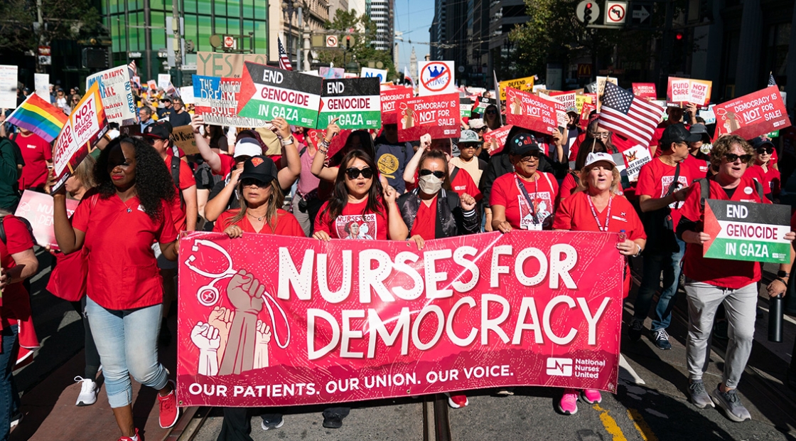 Nurse marching in street holding banner "Nurses for Democracy"