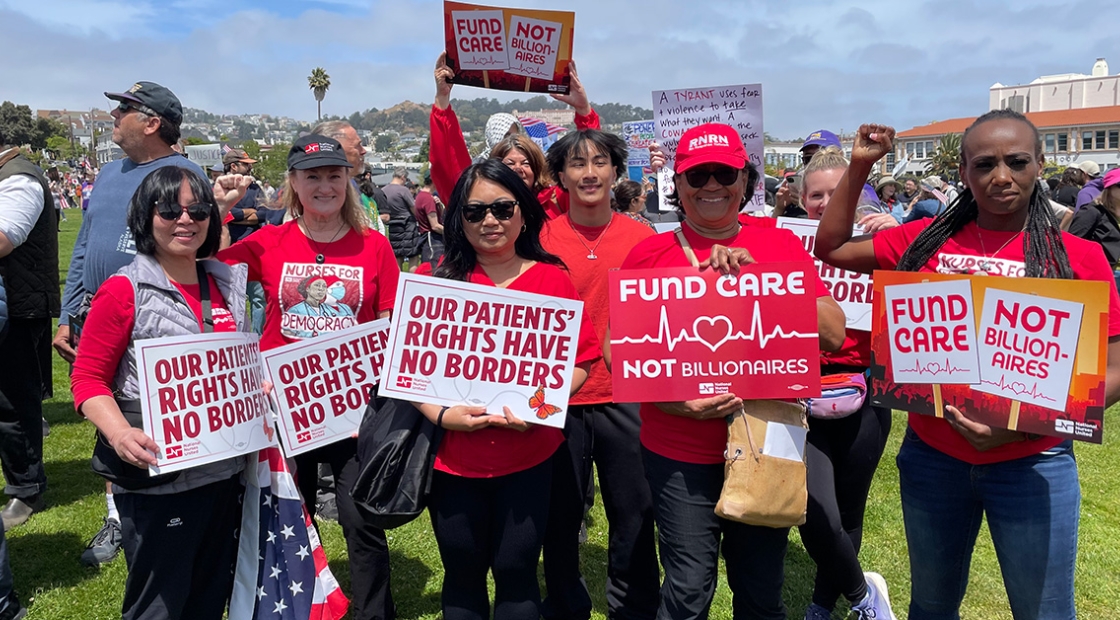 Group of nurses outside, holding signs "Our Patients Rights Have No Borders"