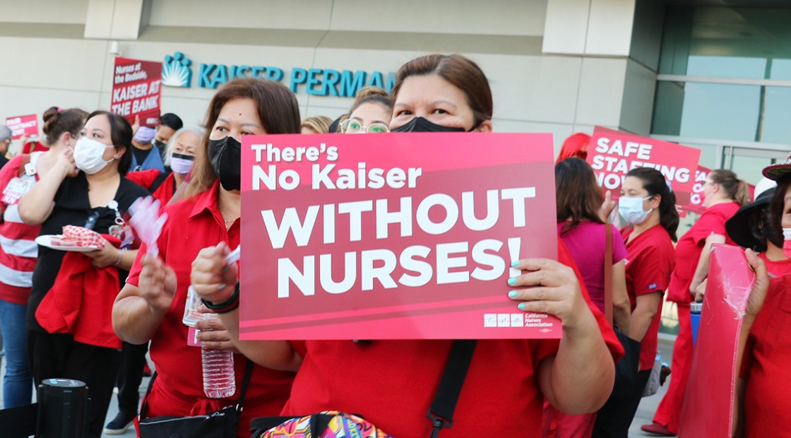 Nurse outside holds sign "There's no Kaiser without nurses"