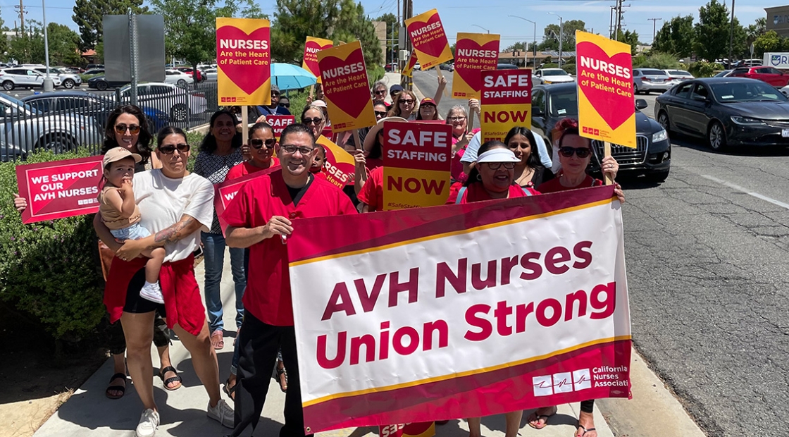 Group of nurses walking outside holding banner "AVH Nurses Union Strong" and signs "Nurses are the heart of patient care"