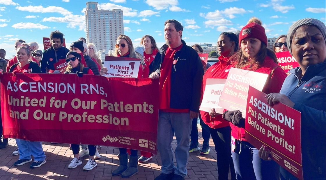 Group of nurses outside holding banner, signs "Ascension, put patients before profits"