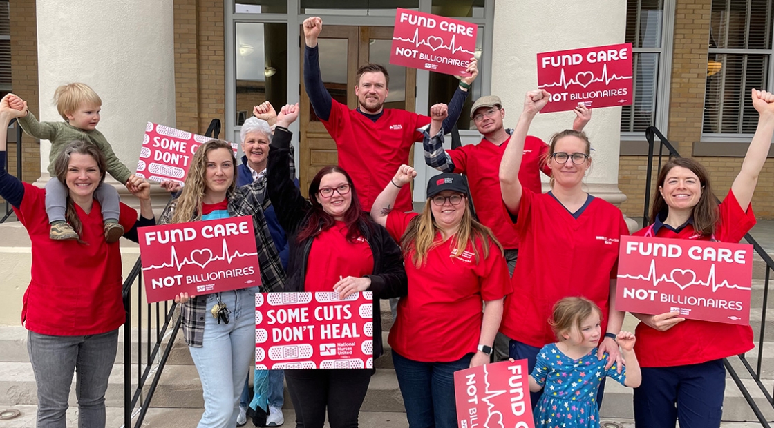 Group of nurses outside in rain clothes holding signs "Some Cuts Don't Heal" and "Fund Care Not Billionaires"