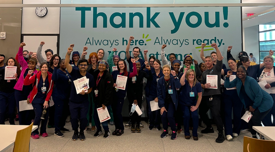 Large group of nurses inside hospital smiling, with raised fists