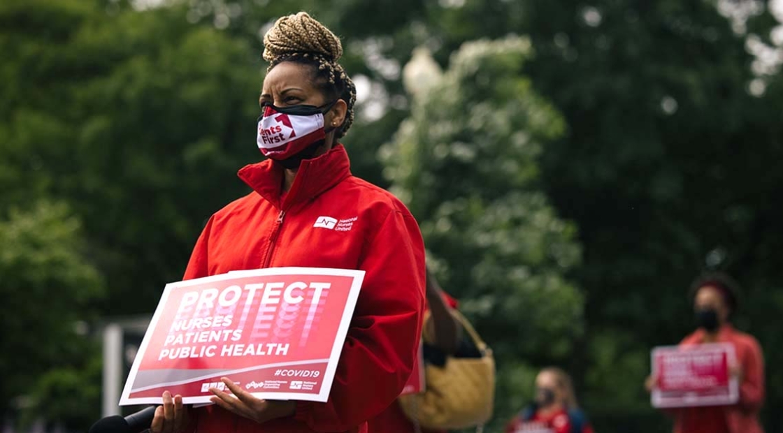 Masked nurse outside holds signs "Protect Nurses, Patients, Public Health"