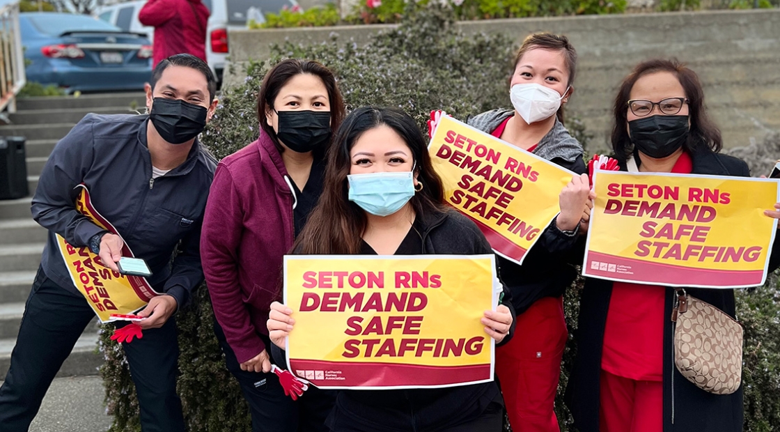Group of five nurses outside Seton Medical Center, holding signs "Seton RNs Demand Safe Staffing"