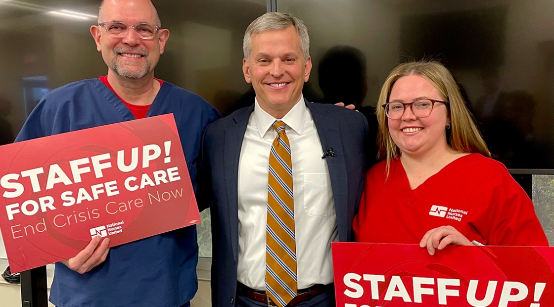 Two nurses standing with North Carolina Attorney General Josh Stein holding signs "Staff Up for Safe Patient Care"