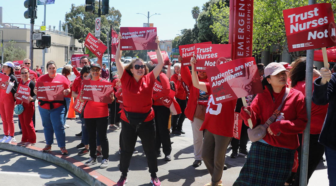 Nurses picketing outside hospital, holding signs "Patients are not algrorithms"