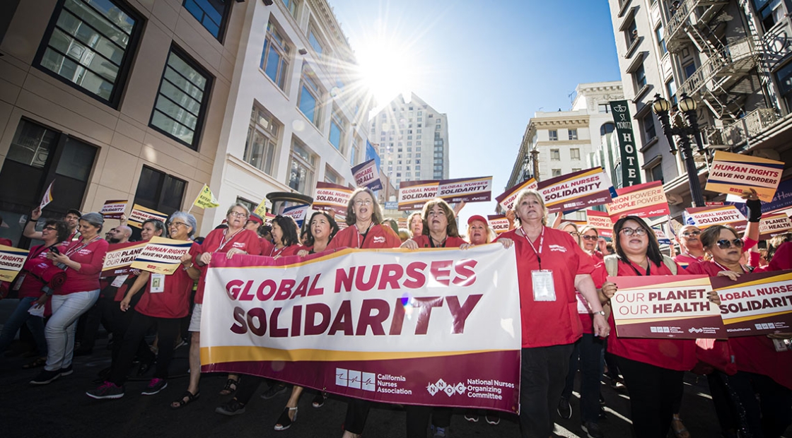 Nurses marching, holding banner that reads "Global Nurses Solidarity" and sign that reads "Our Planet, Our Health"