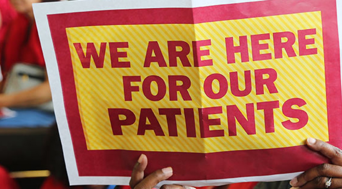 Nurse holding up sign that reads "We are here for our patients."