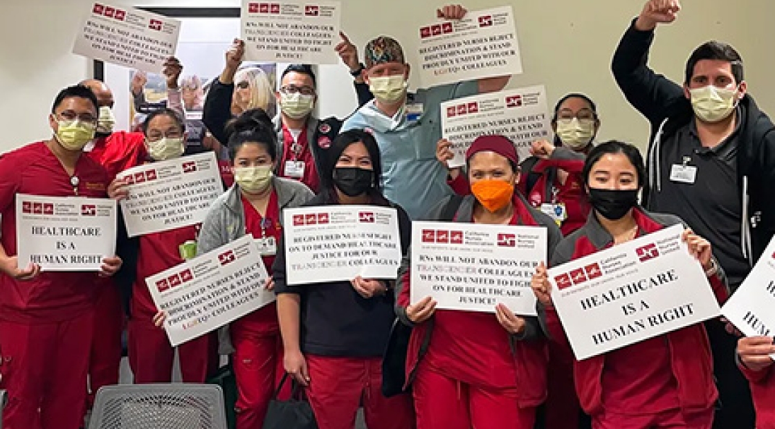 Large group of nurses inside hospital hold signs "Health care is a human right" with raised fists