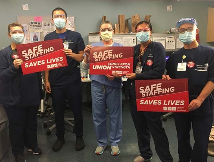 Group of nurses inside hospital hold signs "Safe Staffing Saves Lives"