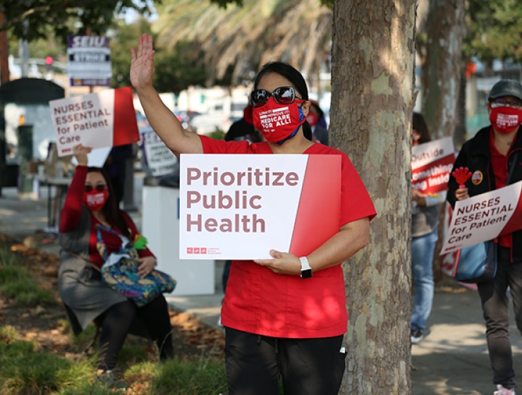 Nurse outside holds sign "Prioritize Public Health"