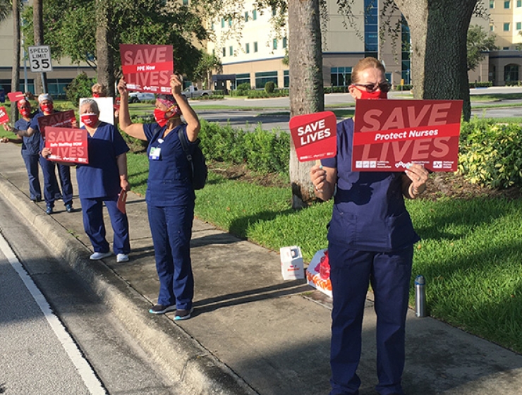 Nurses along road hold signs "Save Lives: Protect Nurses"