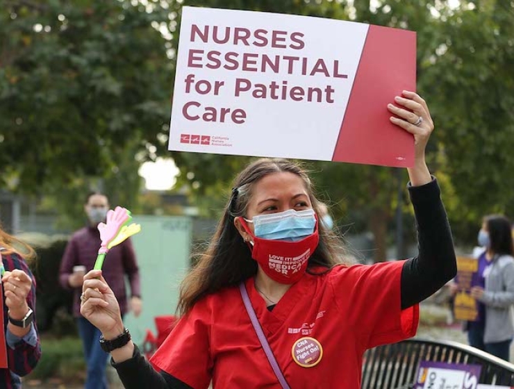 Nurse outside holds sign "Nurses Essential to Patient Care"