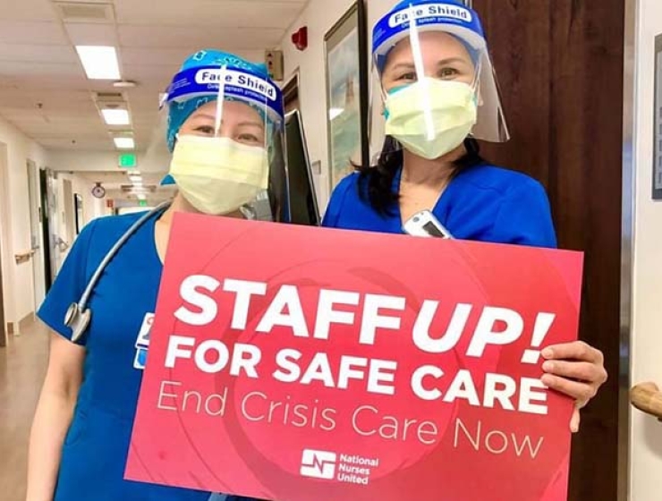 Nurses inside hospital hold signs "Staff Up for Safe Care"
