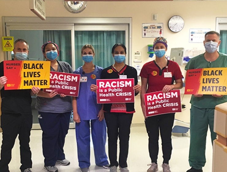 Group of nurses inside hospital hold signs "Racism is a public health crisis" and "Black Lives Matter"
