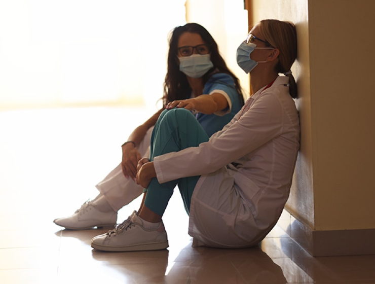Two nurses sitting on floor of hallway looking distressed