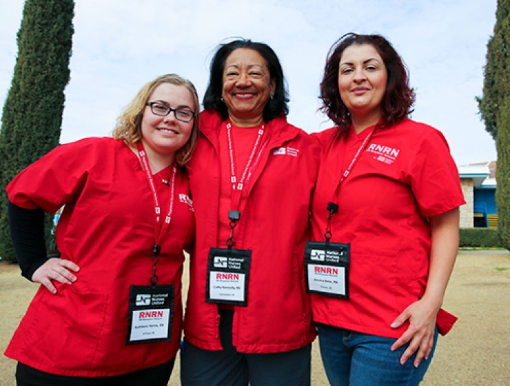 Three nurses wearing RNRN red scrubs standing together with arms around each other.