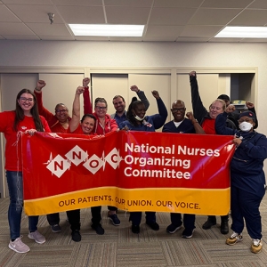 Group of nurses smiling with raised fists, holding banner "National Nurses Organizing Committee"